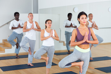 Fototapeta premium Young women and men of different nationalities exercising Hatha yoga poses in modern yoga studio.