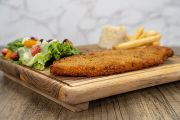 Breaded fish fillet arranged on a wooden platter and served with french fries and salad for a delicious seafood meal