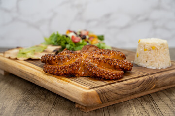 Grilled octopus with legs and tentacles  arranged on a wooden platter and served with rice and salad for a delicious seafood meal
