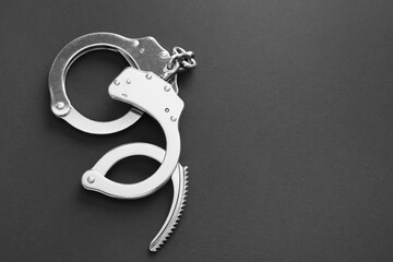 Classic chain handcuffs on black background, top view. Space for text