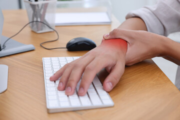 Man suffering from pain in wrist at wooden table, closeup. Office work, Carpal tunnel syndrome