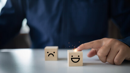 Customer service rating and satisfaction concept, A close-up of a businessman hand selecting a smiley face icon on a wooden cube, leaving a sad face blurred in the background.