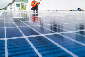 A worker in an orange safety jacket inspects solar panels on a rooftop, using a laptop to ensure...