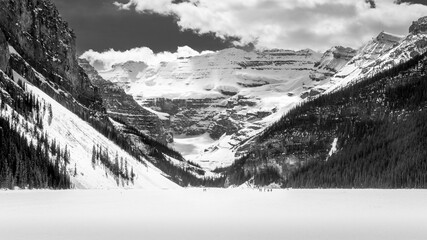 Early May 2024, Lake Louise was still frozen and many people wandered onto the lake. The lake's snow covered surface is surrounded by snow-covered forests and mountains. Black and White Photo