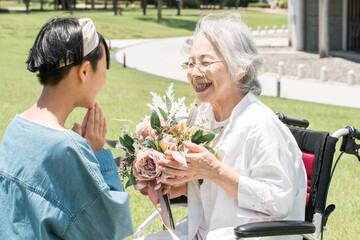 車椅子に乗るおばあちゃんに花束をプレゼントする笑顔の孫娘
