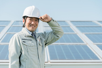 太陽光発電・ソーラーパネルの前に立つ電力会社・電気工事業者の作業着姿の技術者（クリーンエネルギー）

