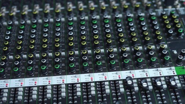 An audio mixer with multiple sliders and knobs being adjusted. The video captures the detailed control of sound levels, perfect for representing audio production, sound engineering, or music creation