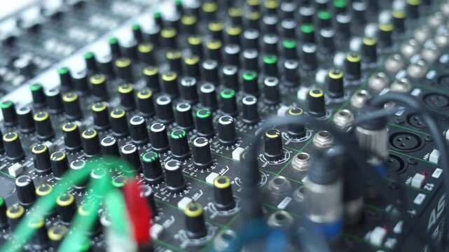 An audio mixer with multiple sliders and knobs being adjusted. The video captures the detailed control of sound levels, perfect for representing audio production, sound engineering, or music creation