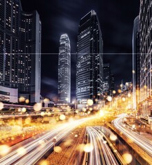 Obraz premium Nighttime view of Hong Kong's cityscape, showcasing towering skyscrapers illuminated with lights against a dark sky. A bustling freeway with bright streaks of light from moving cars can be seen below