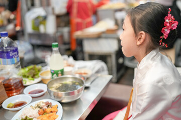 A 9-year-old Korean girl wearing a hanbok is eating a meal at a local market in Changgyeonggung-ro, Jongno District, Seoul, Korea.