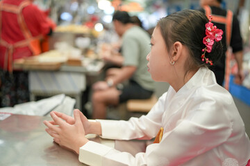 A 9-year-old Korean girl wearing a hanbok is eating a meal at a local market in Changgyeonggung-ro, Jongno District, Seoul, Korea.