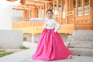 Obraz premium A 9-year-old Korean girl wearing a hanbok is performing a traditional dance in front of a traditional building in the historic town of Gyedong-gil, Jongno District, Seoul, Korea.