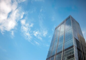 Modern skyscraper against a clear blue sky with fluffy clouds.