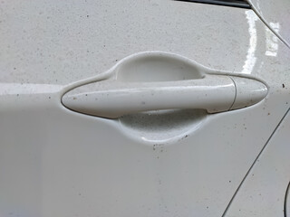 The white car door handle is coated with a fine layer of dust, slightly muting its once glossy finish. The dust clings to the edges and crevices.