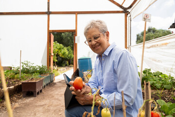 A woman is sitting in a greenhouse with a tomato in her hand. She is smiling and she is enjoying her time