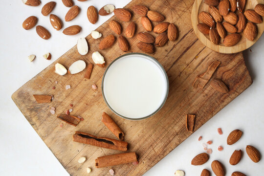 A glass of vegan almond milk on a wooden table, with whole almonds around. Non dairy milk, almond milk, vegan product.