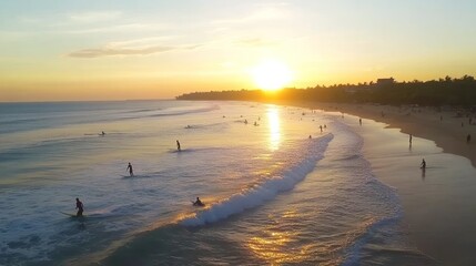 An aerial view of surfers riding waves at sunset on a tropical beach.