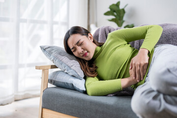 Fototapeta premium Young woman lying on sofa suffering from strong stomach ache