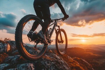 Naklejka premium A mountain biker rides along a ridge at sunset, with a dramatic view of the valley below.