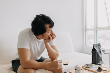 Vacant absent minded Asian man staring out the windows, holding a coffee cup.