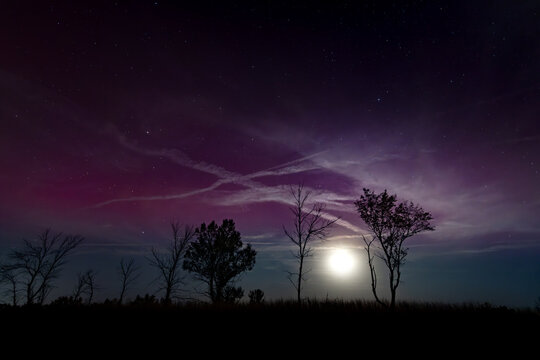 A moonlit evening with purple northern lights high in the atmosphere and the moon illuminating jet streams and clouds over prairie grass savannah at Frontenac State Park in Minnesota