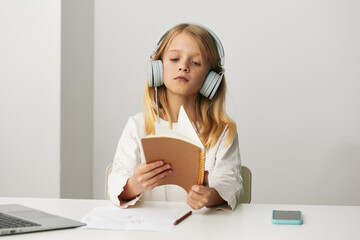 Indoor, a cute caucasian girl sitting at a desk with a laptop, headphones on, and a smile on her face She is immersed in an elearning environment, typing on the computer and enjoying her virtual