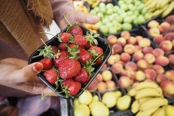 Close up of hands taking small plastic box of fresh strawberries in store..