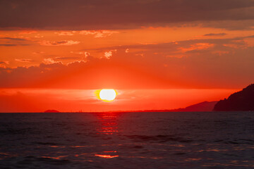 Photo a bright red sun at sunset with clouds, mountains in the sea