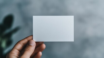 Fototapeta premium Close up of a Hand Holding a Blank Business Card in a Blurred Office Setting