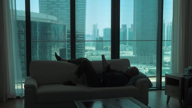 Man in silhouette lying on a couch reading a book in a downtown city apartment