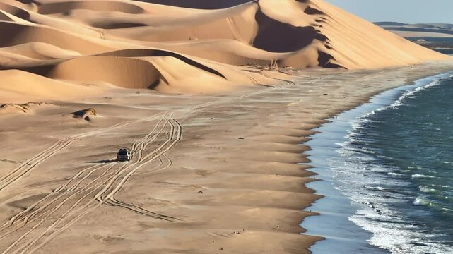 Aerial drone view of a 4x4 driving along the ocean shore beaches next to the Namib dunes on a beautiful day of adventure at sunset, Namibia, Africa