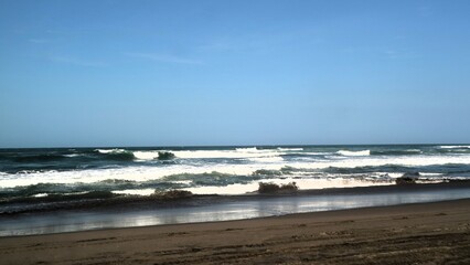 Waves crashing against the shore with a clear blue sky in the background at Parangtritis Beach, Yogyakarta.