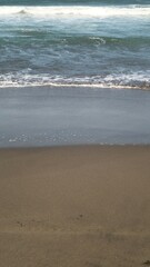 Waves crashing against the shore with a clear blue sky in the background at Parangtritis Beach, Yogyakarta.