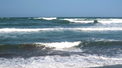 Waves crashing against the shore with a clear blue sky in the background at Parangtritis Beach, Yogyakarta.
