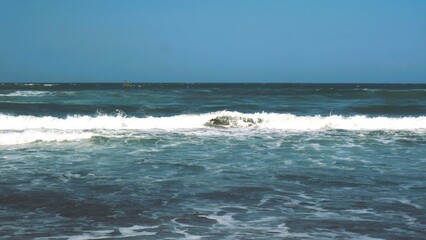 Waves crashing against the shore with a clear blue sky in the background at Parangtritis Beach, Yogyakarta.
