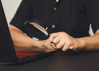 Hand holding magnifying glass over computer keyboard.