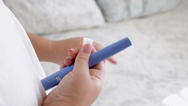 A young woman screws a needle on pre-filled pen injector to prepare it for taking medicine