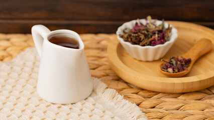 A white jug of Ecuadorian horchata tea served with dried herbs in a ceramic bowl and a wooden spoon on a woven mat. Perfect for promoting traditional drinks, herbal remedies, and organic products.
