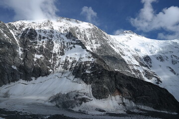 A stunning rock formation covered in snow, set against a clear blue sky with fluffy clouds in the background, creating a peaceful and breathtaking mountain landscape.