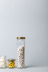 Organic dietary supplements, many capsules of vitamins and minerals in small glass jars on grey background. Nutritional supplements, pills and tablets. Healthy lifestyle.