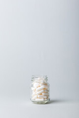 Organic dietary supplements, vitamins and minerals pills in small glass jar on grey background. White capsules in a jar.
