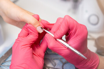 Manicurist applies a base coat of gel polish on woman fingernail using a brush in beauty salon.