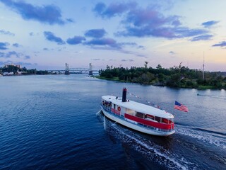 Obraz premium Tourist ferry boat on the Cape Fear River and the Cape Fear Memorial Bridge at sunset in Wilmington, North Carolina, United States.