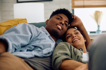 Relaxed multiracial couple watching TV while lying down on sofa.