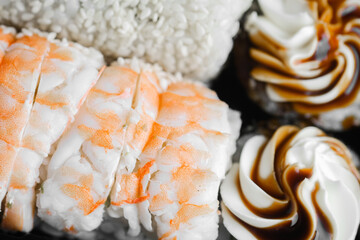Delicious sushi rolls with shrimp and creamy dessert toppings served on a black plate
