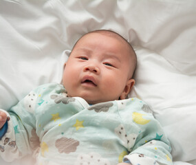 Close-up of male newborn baby wearing hat on his head with relaxed and happy smiling face lying on white bed.