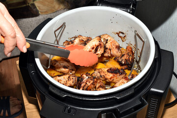 The picture shows a woman's hands using tongs to turn hot chicken meat over in a saucepan.