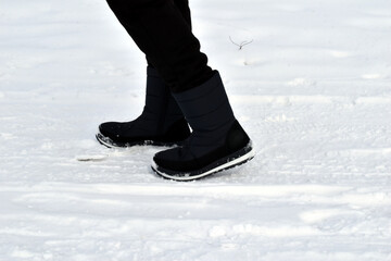 The picture shows the legs of a woman wearing warm shoes and walking through the snow.