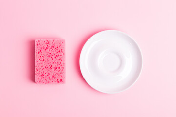 Pink kitchen sponge for washing dishes  and clean white plate on a pink background, top view. Homework. Household work. Washing dishes.