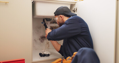 Plumber, man and tools for pipeline in kitchen with home maintenance service and fixing leak by...